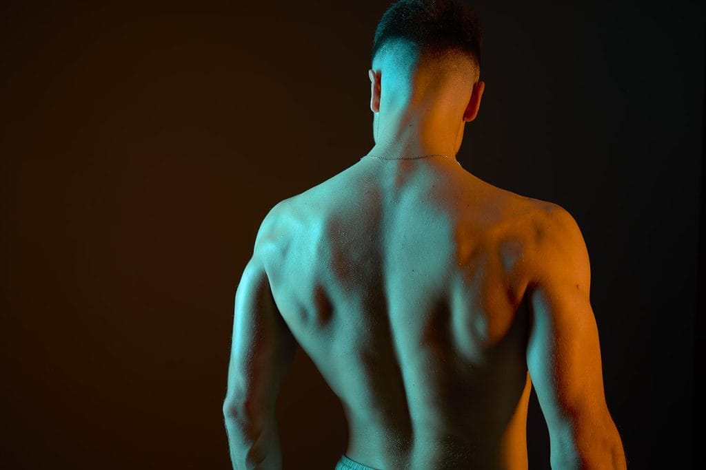 Portrait d'un jeune gymnaste avec des lumières colorées par des gélatines. Vue de dos.