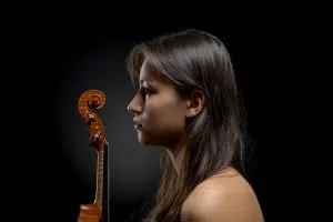 Photographie couleur d'une musicienne avec son violon. Pose assise, ambiance low key, schéma de lumière contre jour.