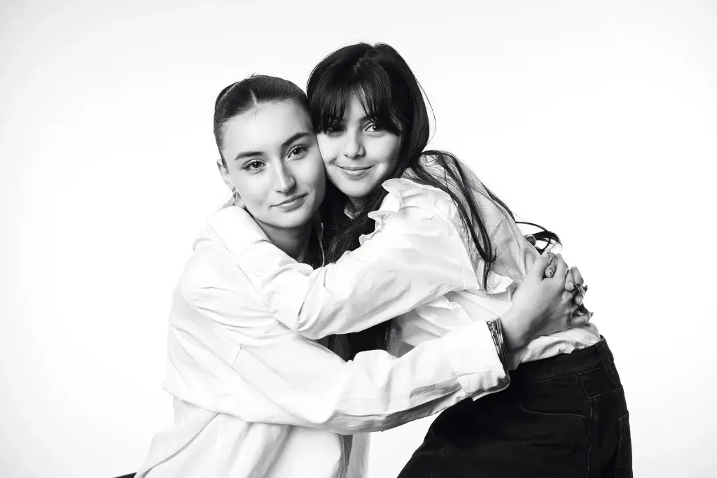 Portrait de 2 sœurs en noir et blanc. Plan taille, lumière douce et contrastée. Visages souriants. Fond blanc