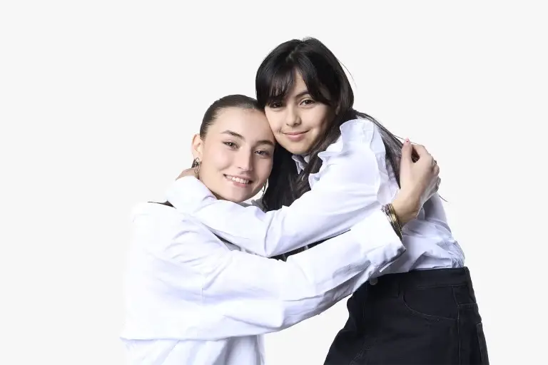 Portrait de 2 soeurs en couleur. Plan taille, lumière douce et contrastée. Visages souriants. Fond blanc