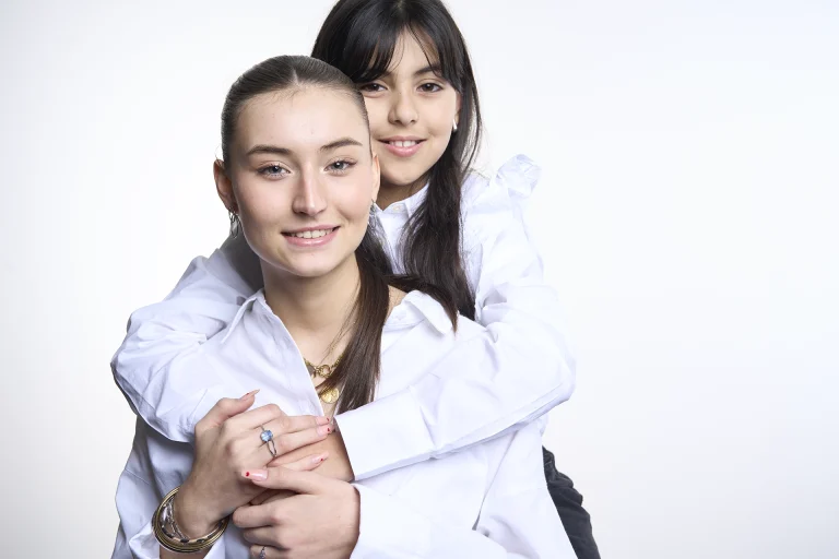 Portrait de 2 soeurs en couleur. Plan taille, lumière douce et contrastée. Visages souriants. Fond blanc