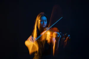 Portrait en couleur d'une jeune femme avec son violon. Utilisation de gélatines colorées pour créer un effet créatif. Dominante de bleu et d'orange. Portrait Taille. Effets de mouvements artistiques. réalisé au Studio Tajan à Tarbes.