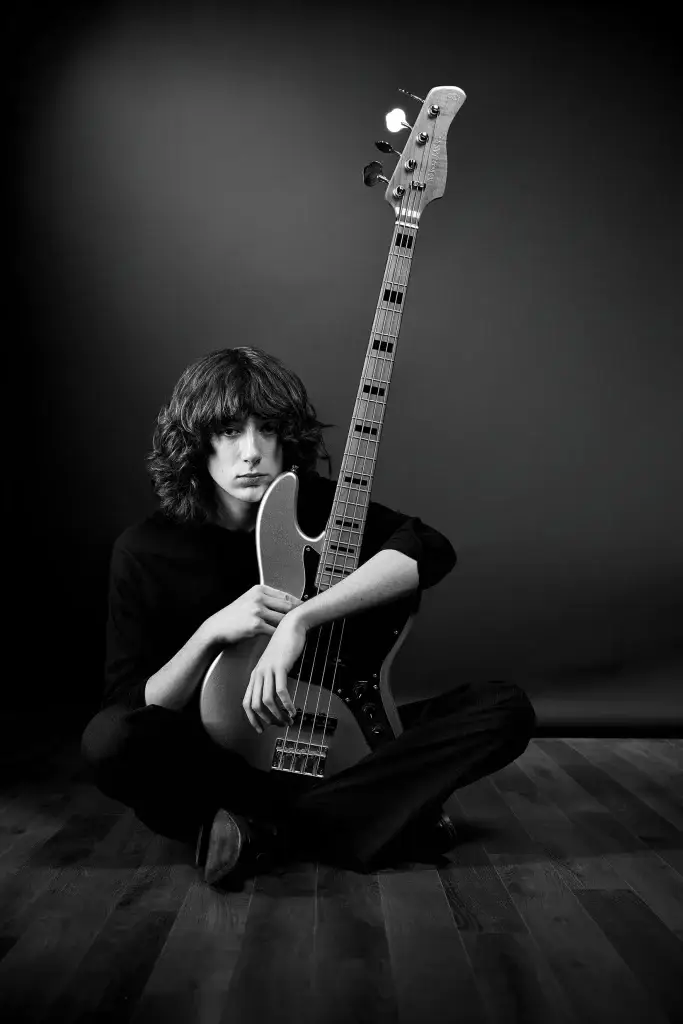 Portrait noir et blanc d'un bassiste assis enlaçant son instrument. Vêtements et fond sombres. Attitude songeuse capturée par le studio Tajan sur Tarbes.