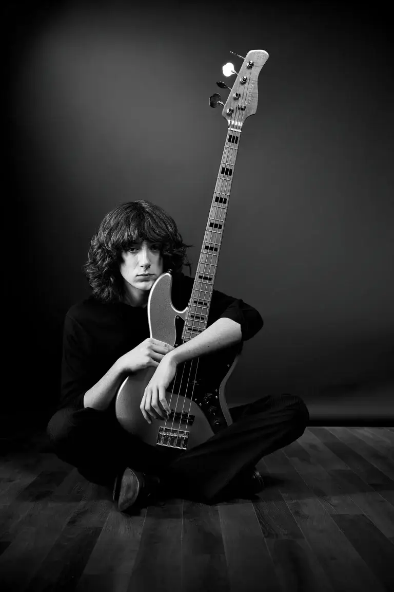 Portrait noir et blanc d'un bassiste assis enlaçant son instrument. Vêtements et fond sombres. Attitude songeuse capturée par le studio Tajan sur Tarbes.