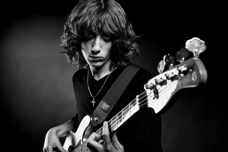 Photographie de portrait d'un bassiste. Gros plan en noir et blanc sur le visage, les mains et la basse. Ambiance sombre donnant du caractère.