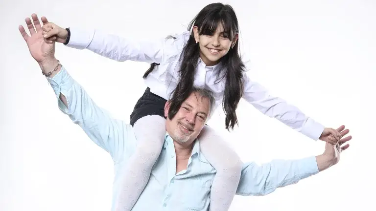Photo de portrait amusante d'un père avec sa fille. Celle-ci est posée sur les épaules de son papa et fait l'avion. séance photo du studio Tajan sur Tarbes.