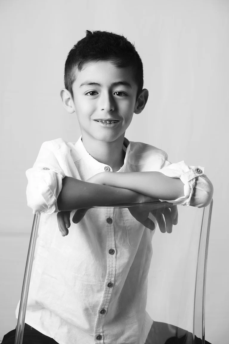 Portrait d'un garçon en noir et blanc. Pose assise, visage souriant. Lumière douce er contrastée.