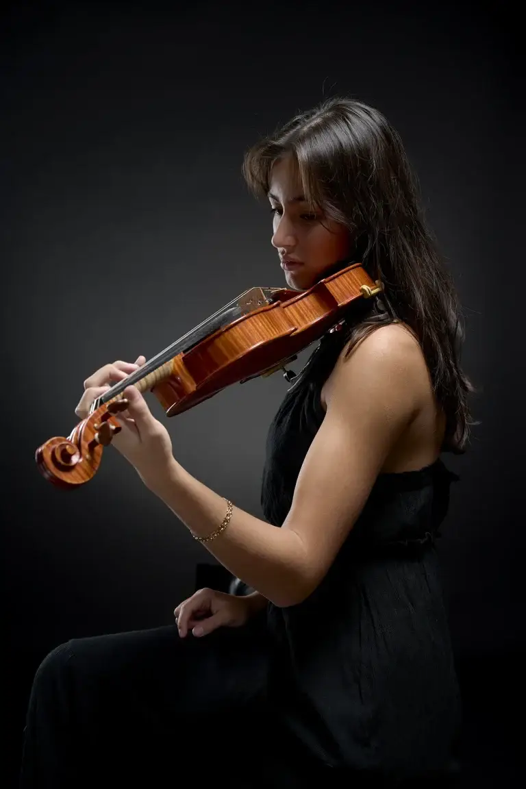 Portrait en contre jour d'une jeune violoniste. Photo de studio mettant en lumière le triangle constitué par le bras et le violon.