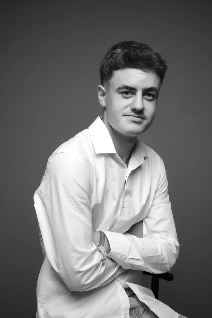 shooting photo avec un jeune homme dans notre studio sur Tarbes. Chemise blanche sur fond sombre. Pose assise.