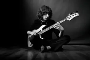 photo d'un musicien en noir et blanc. Le jeune homme est assis et joue de la basse. Décor et vêtements sombres.