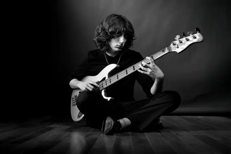 photo d'un musicien en noir et blanc. Le jeune homme est assis et joue de la basse. Décor et vêtements sombres.
