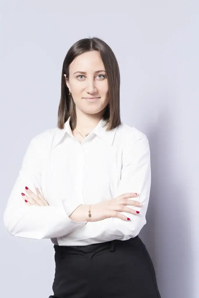 Portrait corporate d'une jeune femme debout, en chemise blanche. Lumière douce et enveloppante mettant en avant son regard et son sourire.
