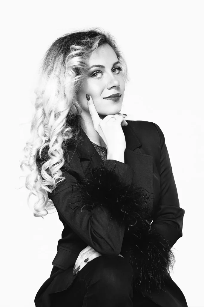 Portrait noir et blanc d'une jeune modele qui pose assise dans une tenue noire. Elle est blonde et la lumière de la scène est très douce.