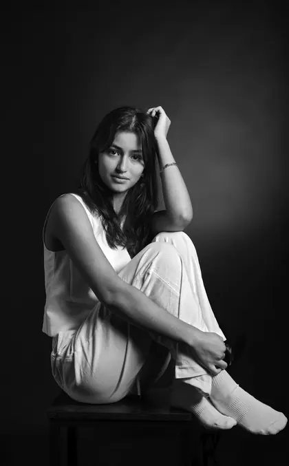 Portrait en noir et blanc d’une jeune femme assise, main dans les cheveux