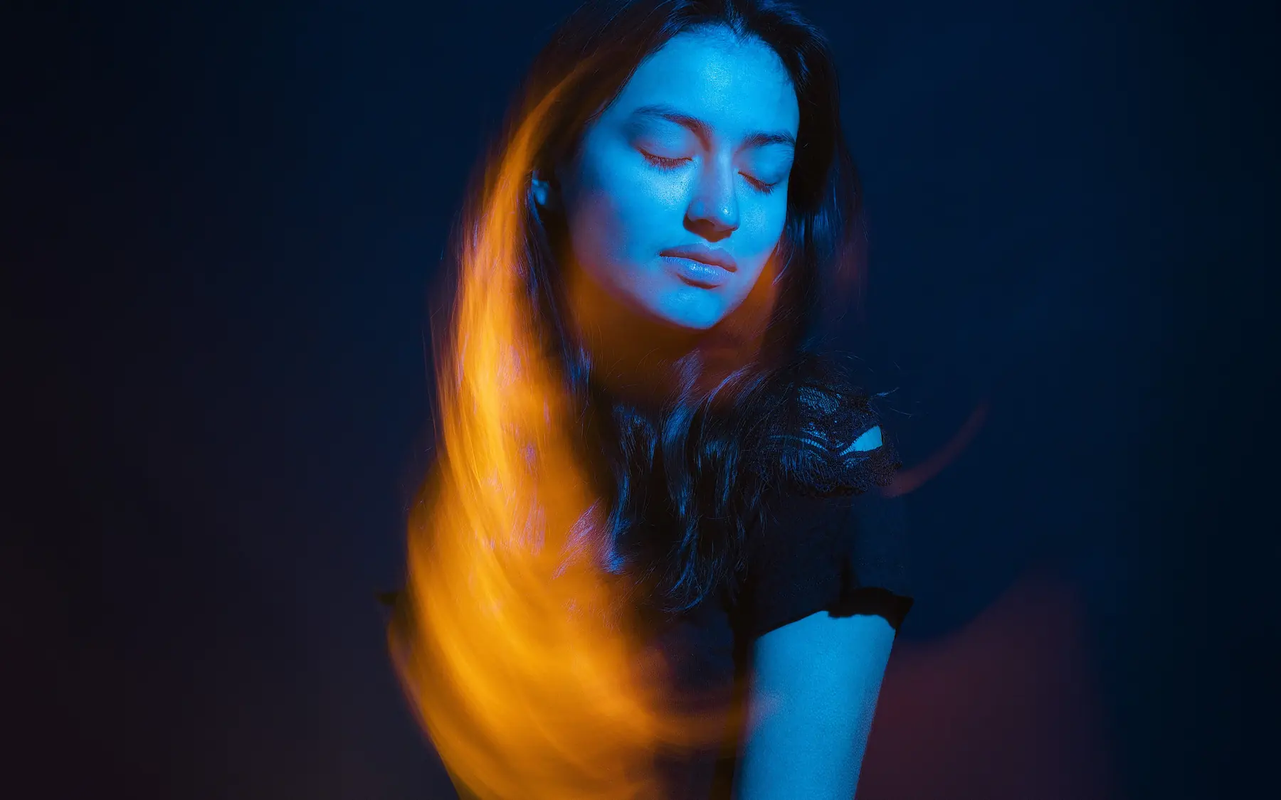 Portrait d’une jeune femme aux yeux fermés en lumière bleue et orangée, au studio à Tarbes