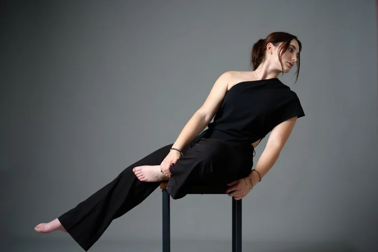 Book modèle couleur : pose étirée sur un tabouret, pantalon noir, fond gris, photographe à Tarbes