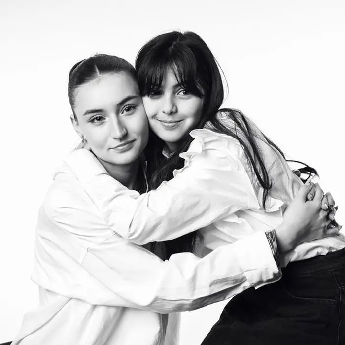 Portrait de studio en noir et blanc : deux sœurs enlacées, chemises blanches, sur fond clair.