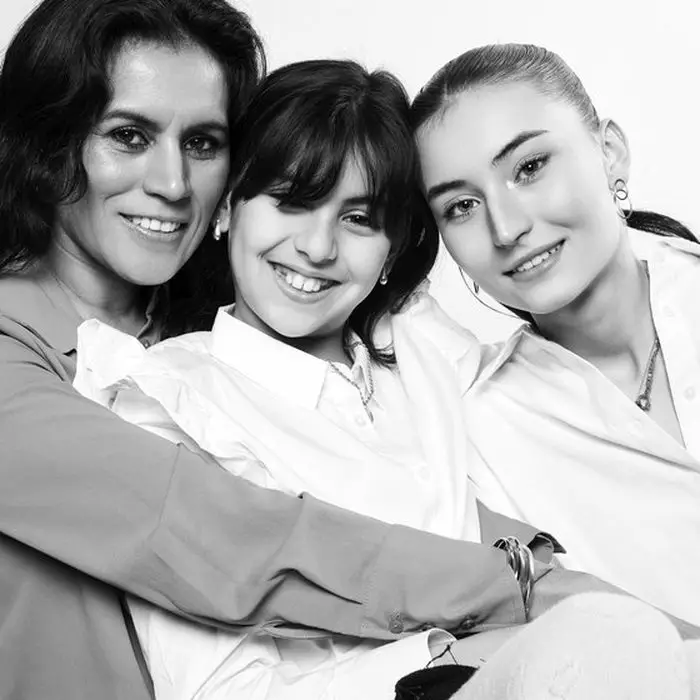 Portrait de studio en noir et blanc : une mère et ses deux filles serrées l'une contre l'autre, vêtues de clair.