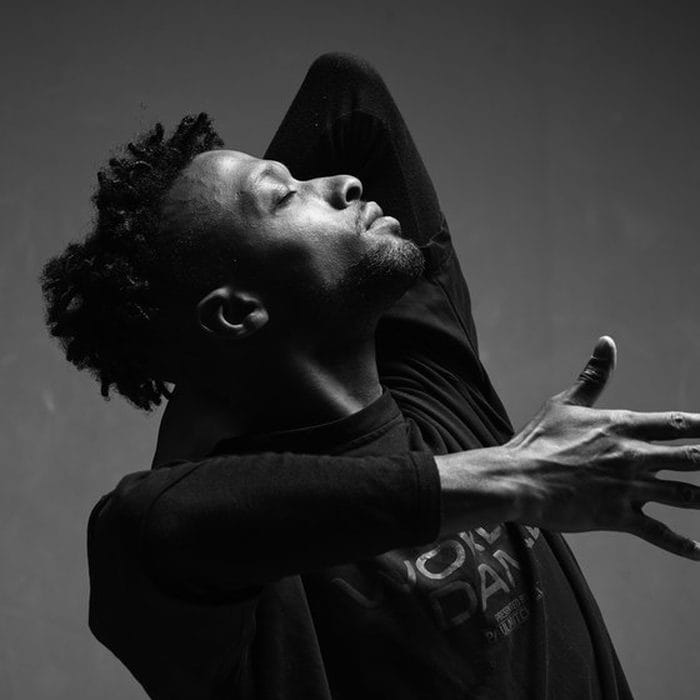 Portrait de studio en noir et blanc : danseur en mouvement, tête renversée en arrière et bras tendu.