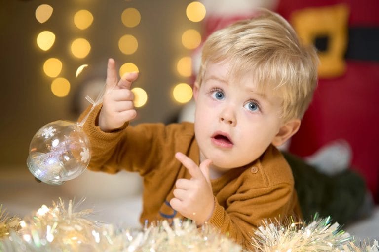 Tout-petit tenant une boule de Noël, lumières dorées en fond