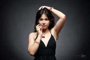 Portrait féminin artistique en couleur, mains contre le visage, robe noire sur fond sombre