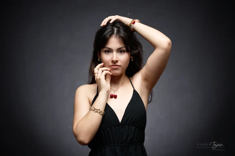 Portrait féminin artistique en couleur, mains contre le visage, robe noire sur fond sombre