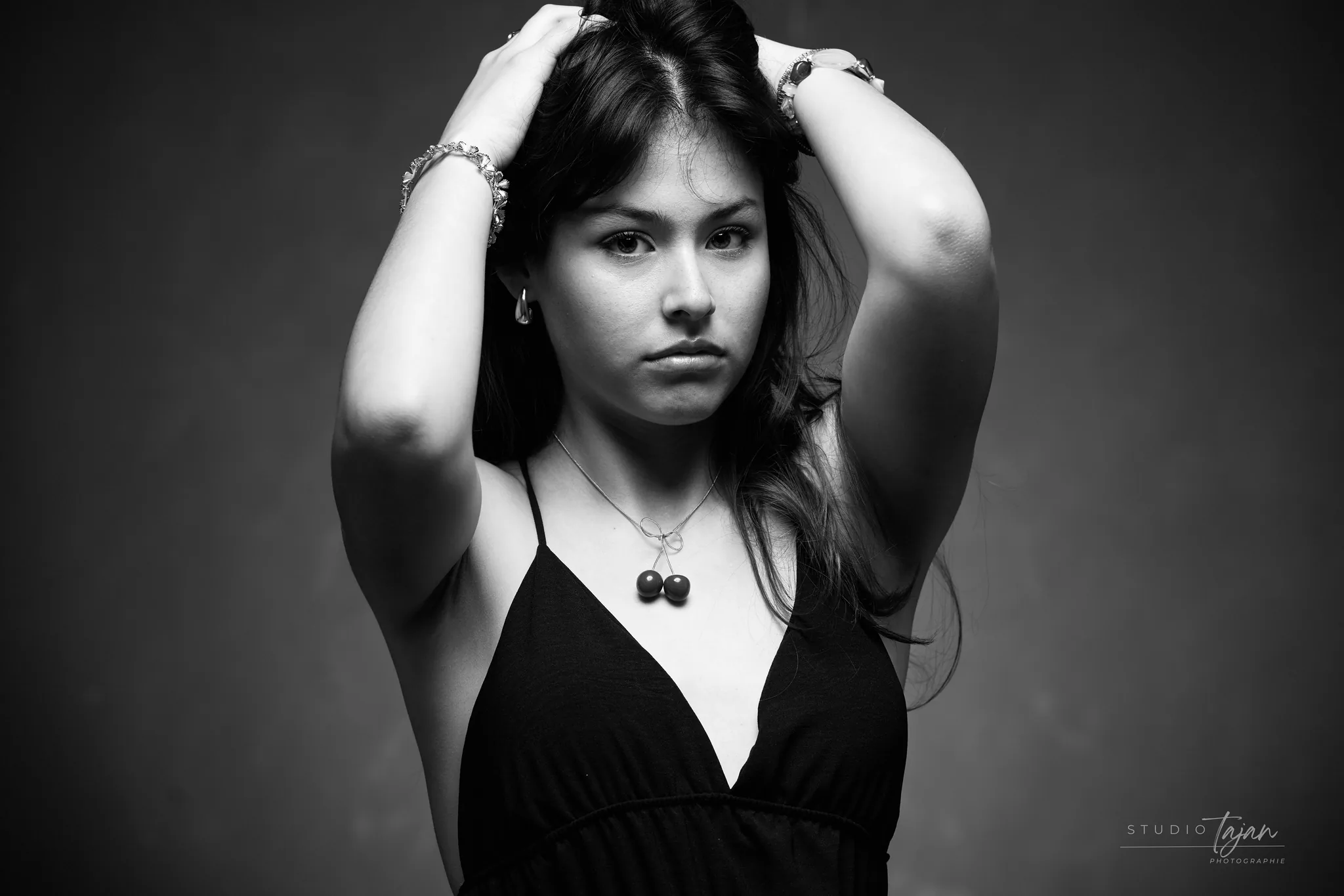 Portrait féminin en noir et blanc, mains dans les cheveux, regard posé