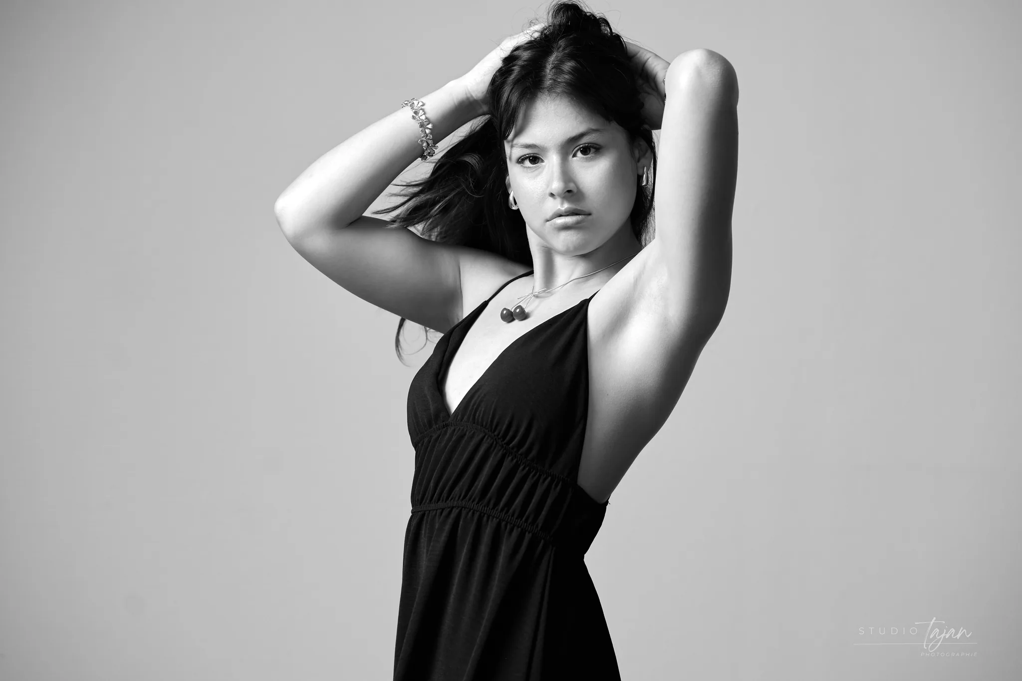 Portrait féminin en noir et blanc sur fond clair, bras levés